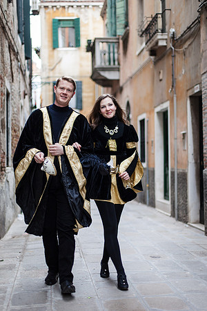 Elegant couple in Venetian carnival costumes walking through a historic street in Venice, Italy.