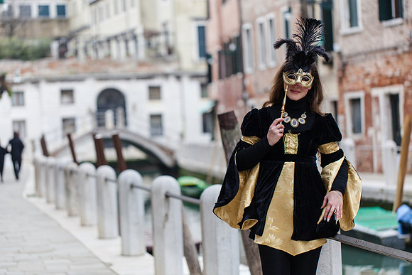 Woman in a black and gold Venetian carnival dress walking across a bridge.