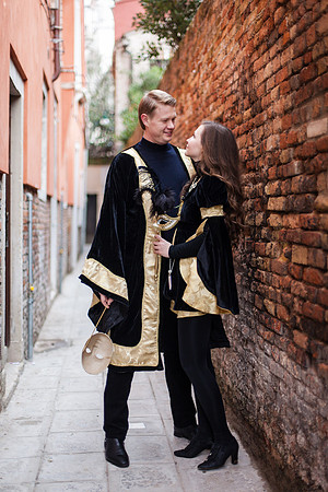 Elegant couple in carnival attire walking through a historic alley.