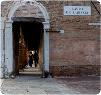 The newly engaged couple walks hand in hand through a charming archway.