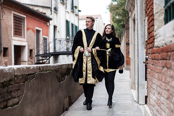 Masked couple in Venetian carnival costumes walking through an atmospheric alley in Venice.