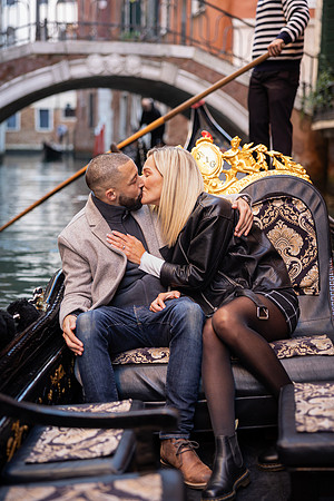 A couple lost in their engagement bliss, sharing a kiss in a traditional Venetian gondola.
