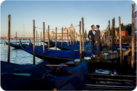 Couple holding hands near gondolas in Venice during sunrise.