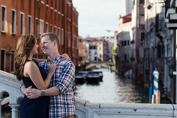 A newly engaged couple shares a tender embrace by a historic Venetian landmark.