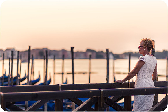 Mother and daughter standing by the gondolas at sunrise, with a golden glow over Venice.