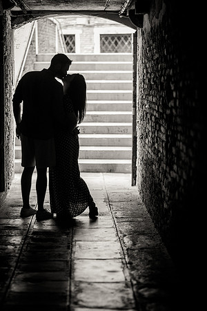 Couple holding hands, walking toward the light in a historic Venice passageway.