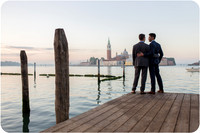 Engaged couple walking along a Venetian dock with gondolas in the background.