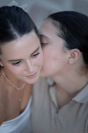 Soft-focus portrait of a same-sex couple, one kissing the other’s cheek.