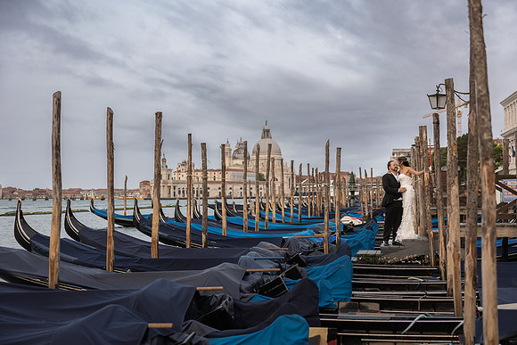Bride in lace gown walking among moored gondolas - Anniversary sunrise photoshoot in Venice.