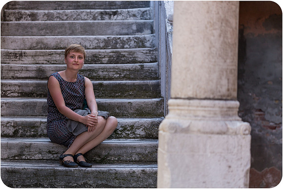 Lesbian woman leaning against a sunlit brick wall in Venice.