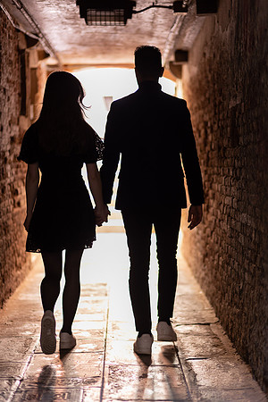 Silhouetted couple walking through a historic Venetian alleyway.