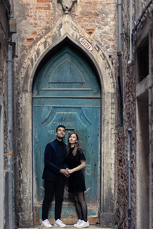 Couple standing in front of an old Venetian door, holding hands.