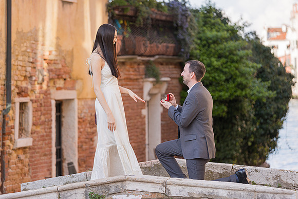 Man proposing on a stone bridge in Venice near greenery.