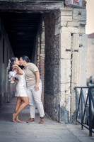 Engaged couple playfully dancing in a shaded Venetian walkway.