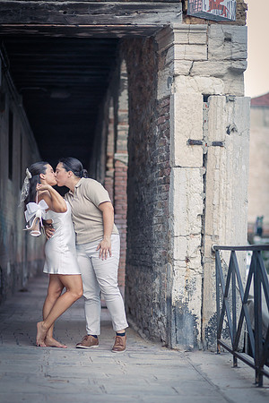 Engaged couple playfully dancing in a shaded Venetian walkway.