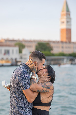 Couple kissing after sunset proposal with St. Mark’s tower in background.