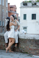 Same-sex couple cuddling on a stone ledge with Venice in the background.