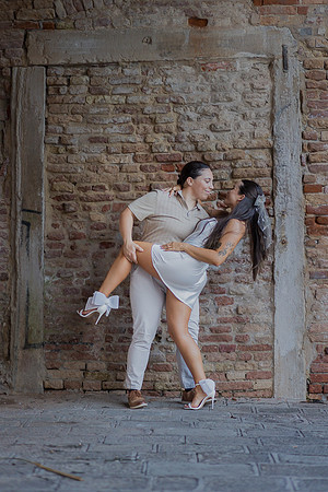 Same-sex couple sharing a playful embrace under an old Venetian arch.