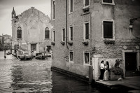 Couple standing by the canal, with historic Venice in the background.