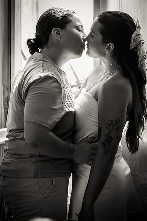 Same-sex couple kissing in a black and white engagement portrait.