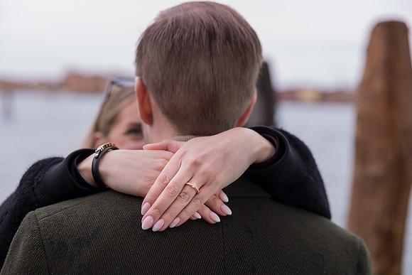 A close-up of the engagement ring as the woman lovingly wraps her arms around her fiancé.