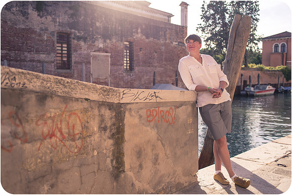 Lesbian woman leaning against a sunlit brick wall in Venice.