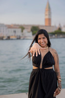 Engaged woman smiling and displaying ring with Venice skyline behind.