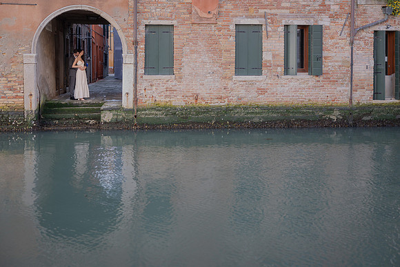 Couple sitting by a Venice canal, reflected in the water.
