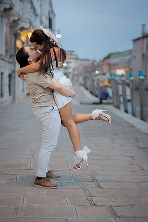 Engaged couple laughing and embracing by a scenic Venice bridge.