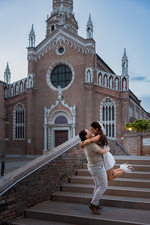 Engaged couple spinning each other playfully in front of a Venetian landmark.