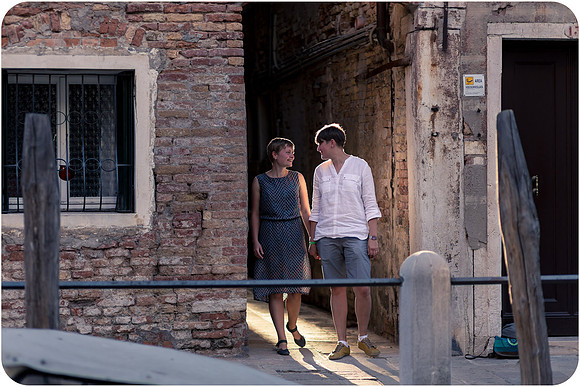 Lesbian couple walking through sunlit Venetian alleys.