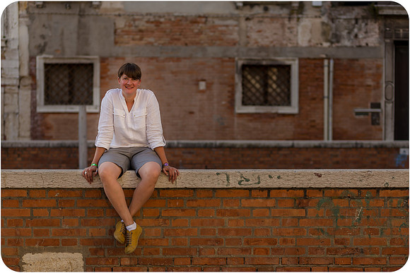 Lesbian woman sitting near a Venetian canal, reflecting during a summer afternoon.